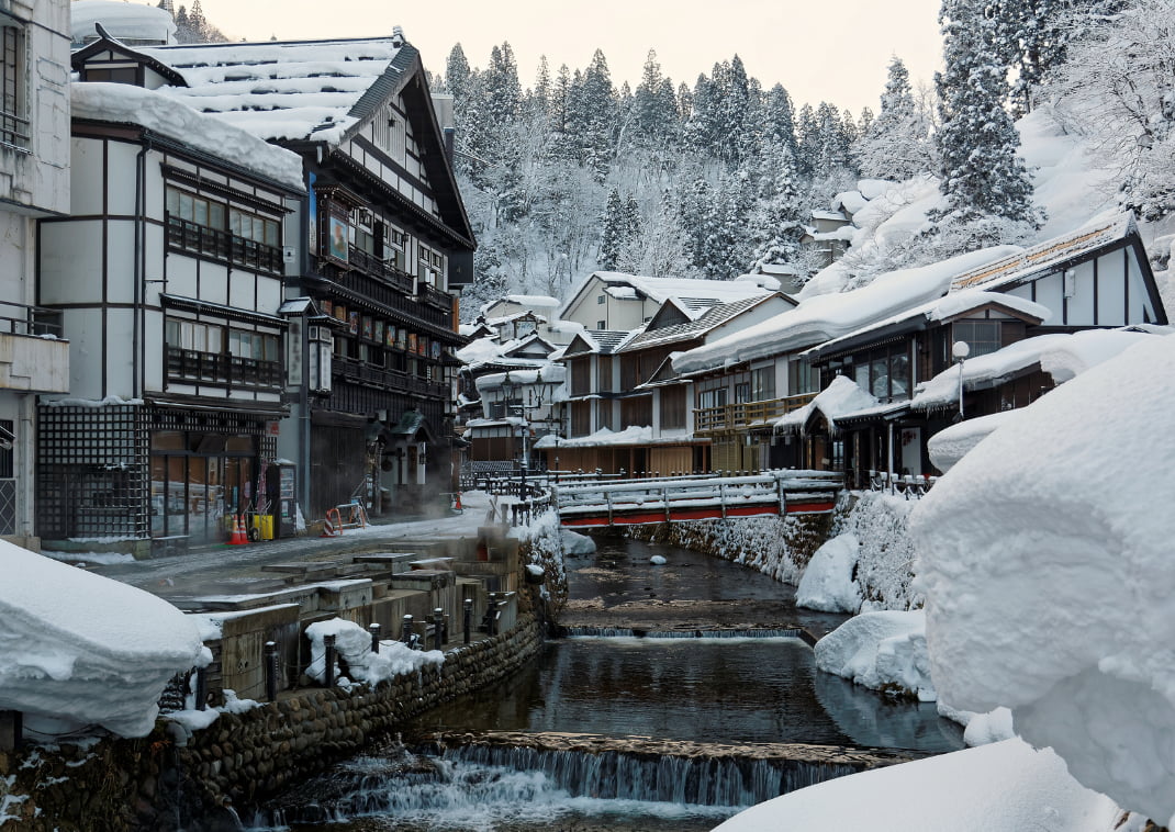 Winter scenery of Ginzan Onsen, a famous Japanese hot spring town in Obanazawa, Yamagata, Japan, with bridges over a stream flanked by historical wooden buildings after heavy snowfalls in the morning