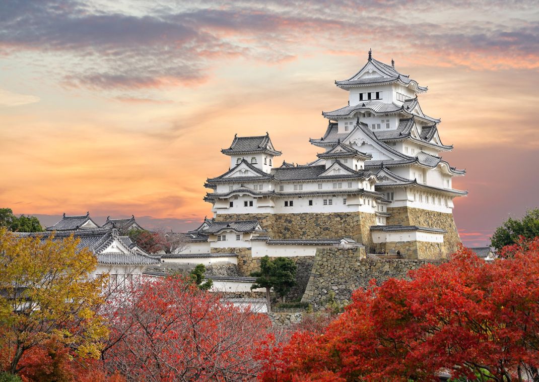 Himeji Castle and red maple leaves in evening sunlight and twilight sky in Himeji city, Hyogo prefecture of Japan