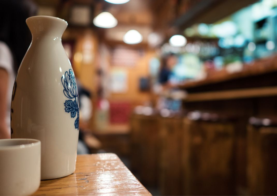 Sake bottle and cup with restaurant out of focus in the background.