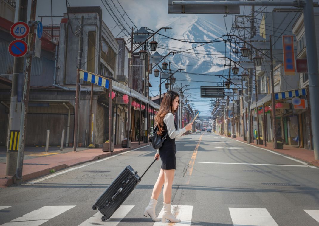 Woman carrying luggage and holding map on a Fujiyoshida street with Mt. Fuji in the background