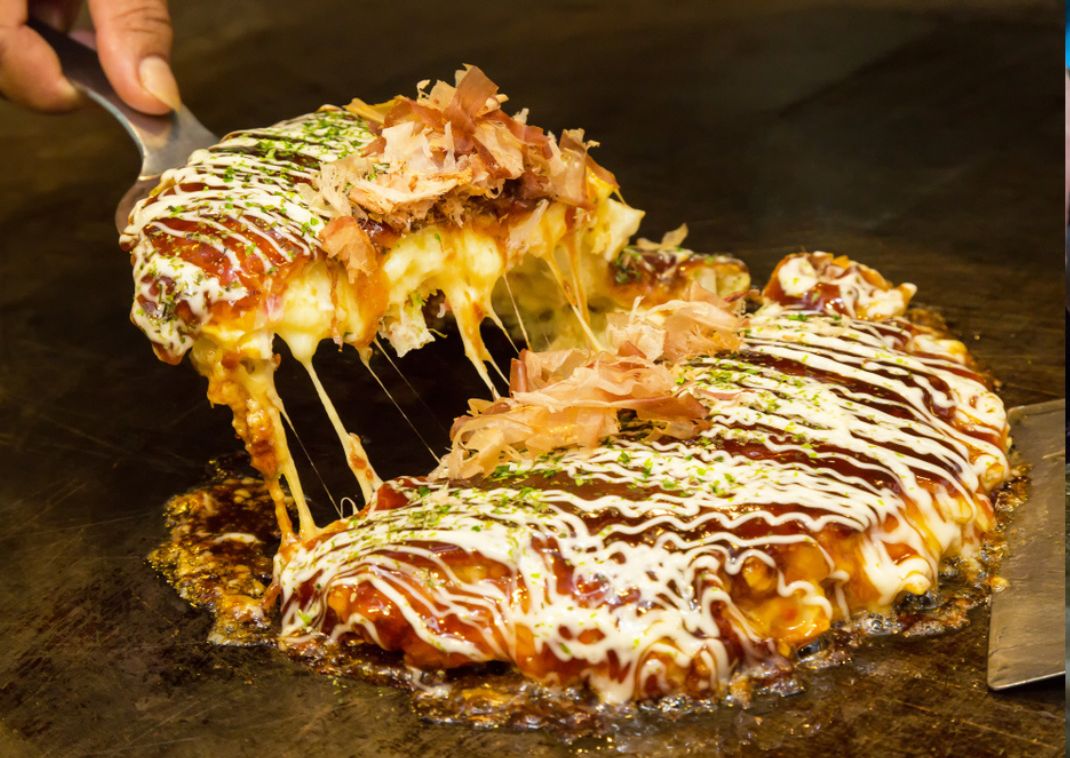 Japanese savory pancake called okonomiyaki being grilled on a hotplate.