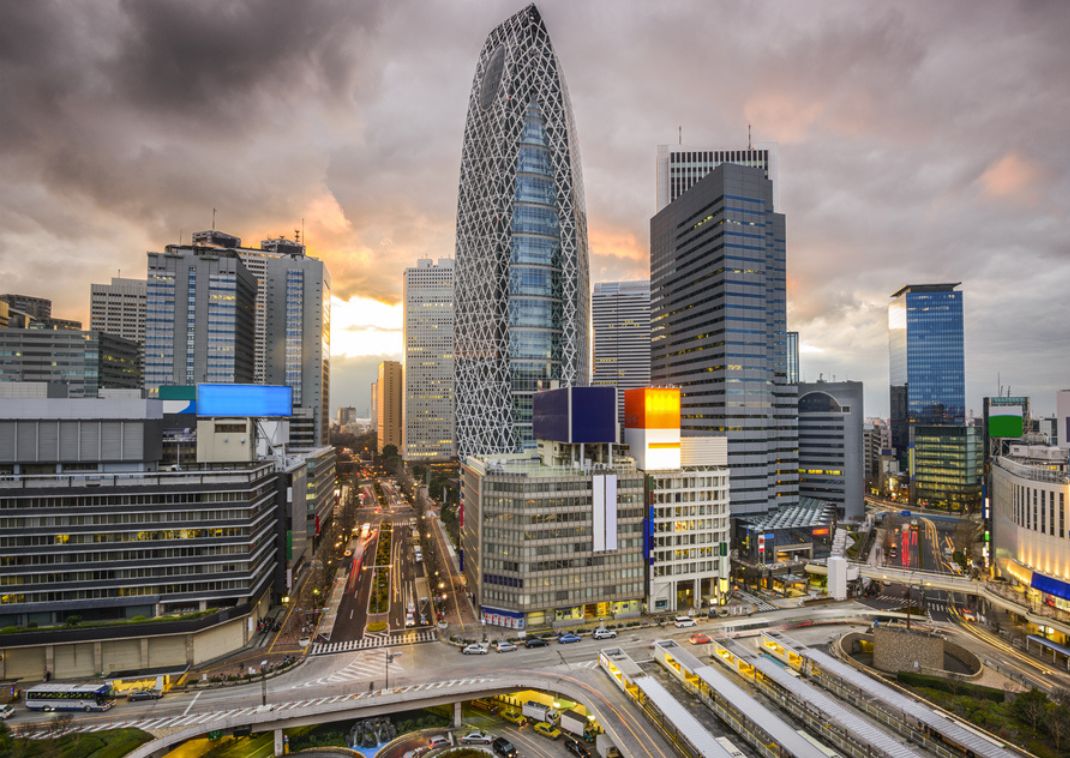 Panoramic view of a Tokyo business district with modern skyscrapers, including the Cocoon Tower, under a cloudy sky at sunset