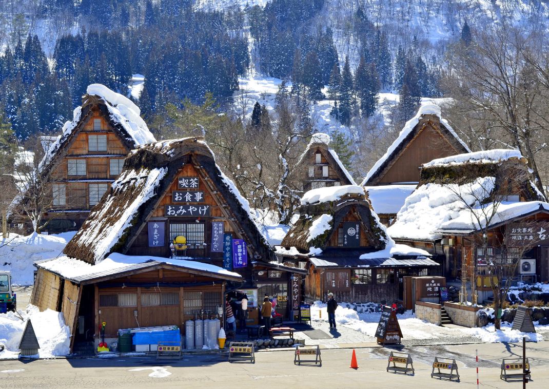 Traditional Gassho-zukuri farmhouses in Gokayama covered in snow, with steep thatched roofs designed for heavy winters, surrounded by mountains and pine trees.