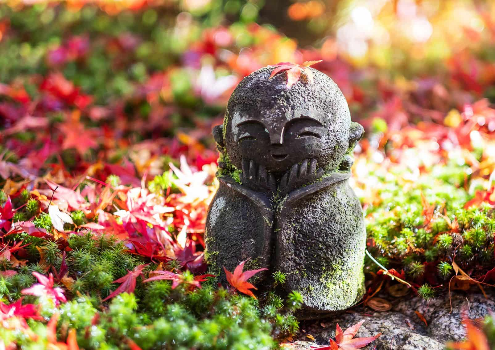 Japanese Jizo sculpture doll with falling Red Maple leaf in Japanese Garden at Enkoji Temple, Kyoto, Japan