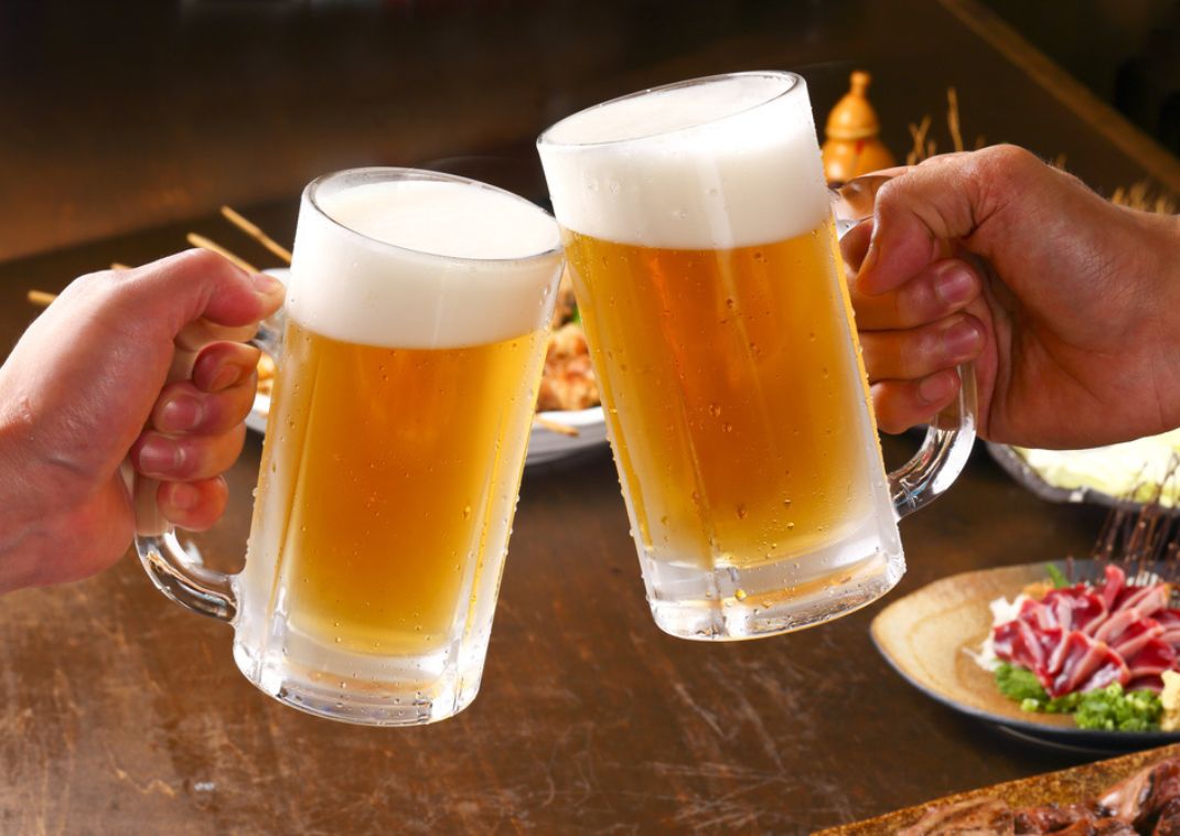 Two hands holding glasses of frothy Japanese beer