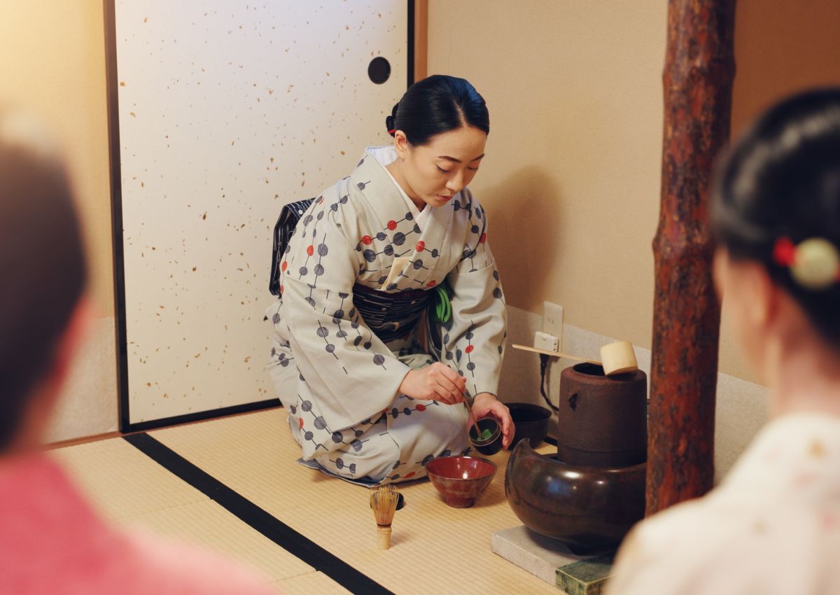Lady in kimono preparing matcha for tea ceremony with guests