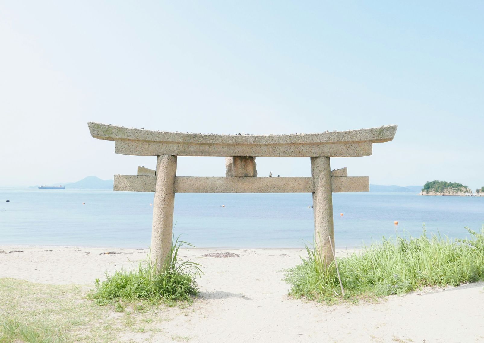 A stone torii gate half submerged in the sand with the sea in the background 