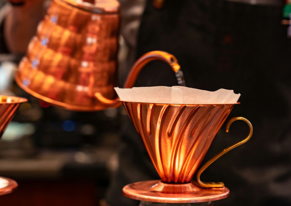 Barista brewing pour-over coffee with a copper kettle and dripper