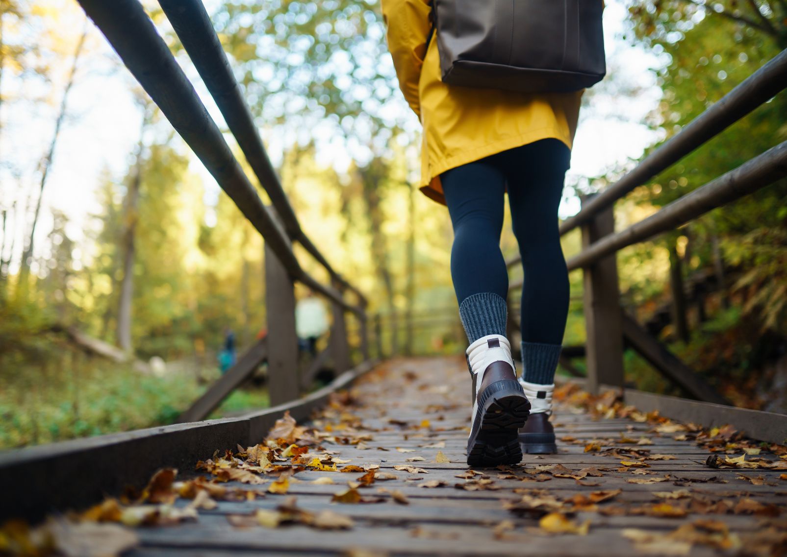 A woman’s boots walking along a wooden trail through an autumn forest