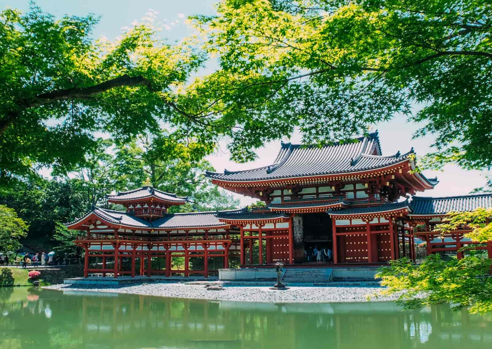  Bright red Byodo-in Temple in Uji, Kyoto, reflected in the water with green maple leaves, Japan