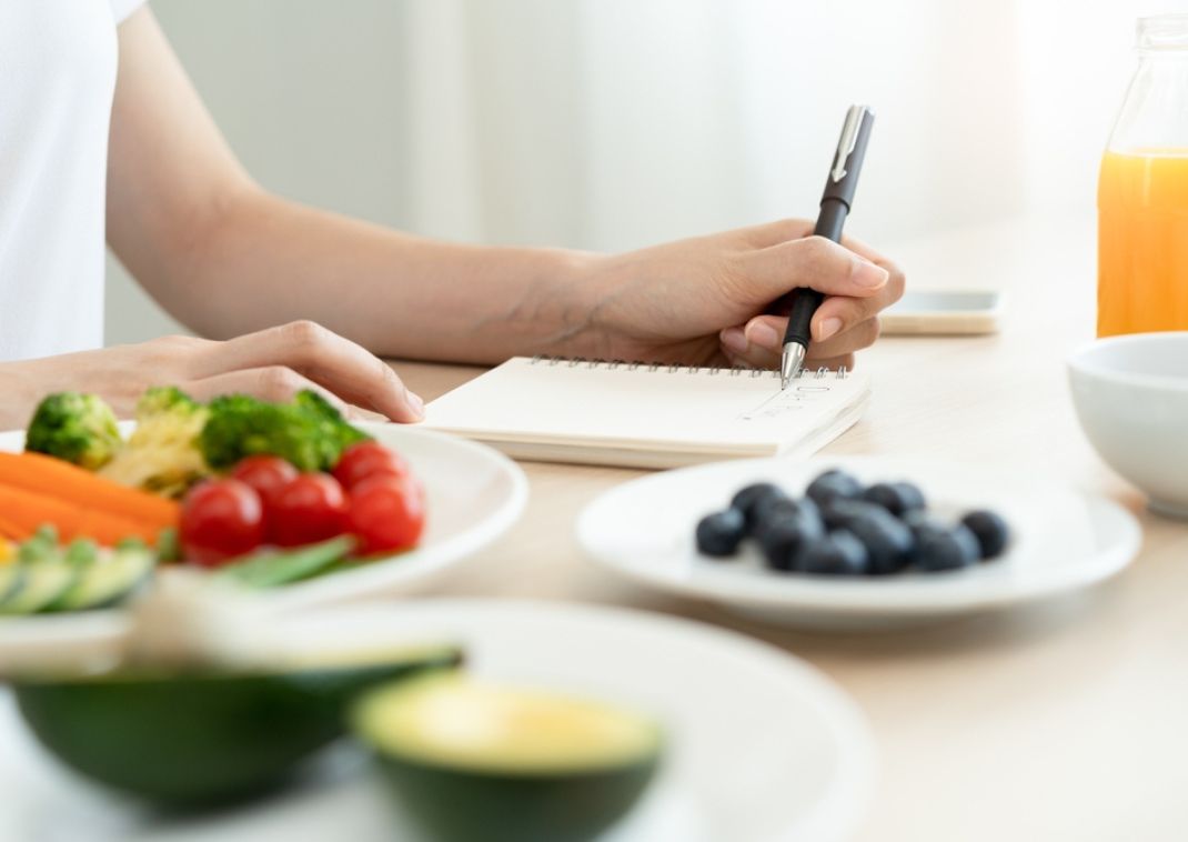Woman writing down words surrounded by healthy fruit