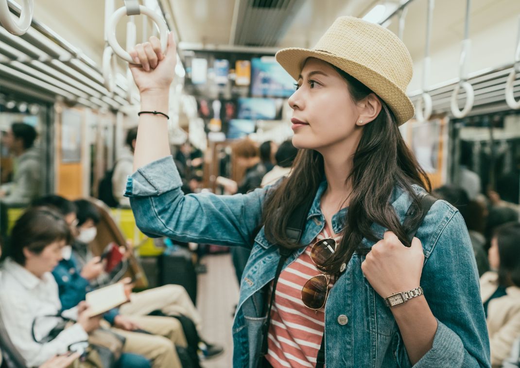 Young female Asian traveler hand holding handle standing on subway train in Japan