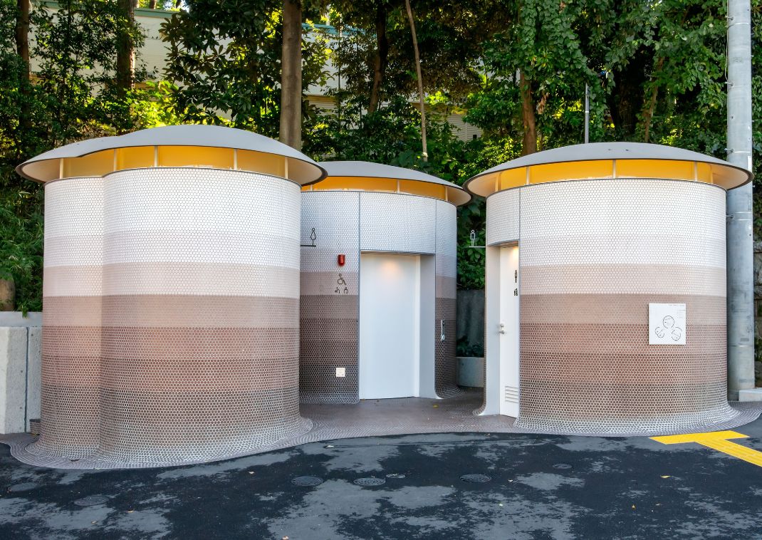 Modern circular public toilets with patterned walls and rounded roofs, surrounded by greenery.