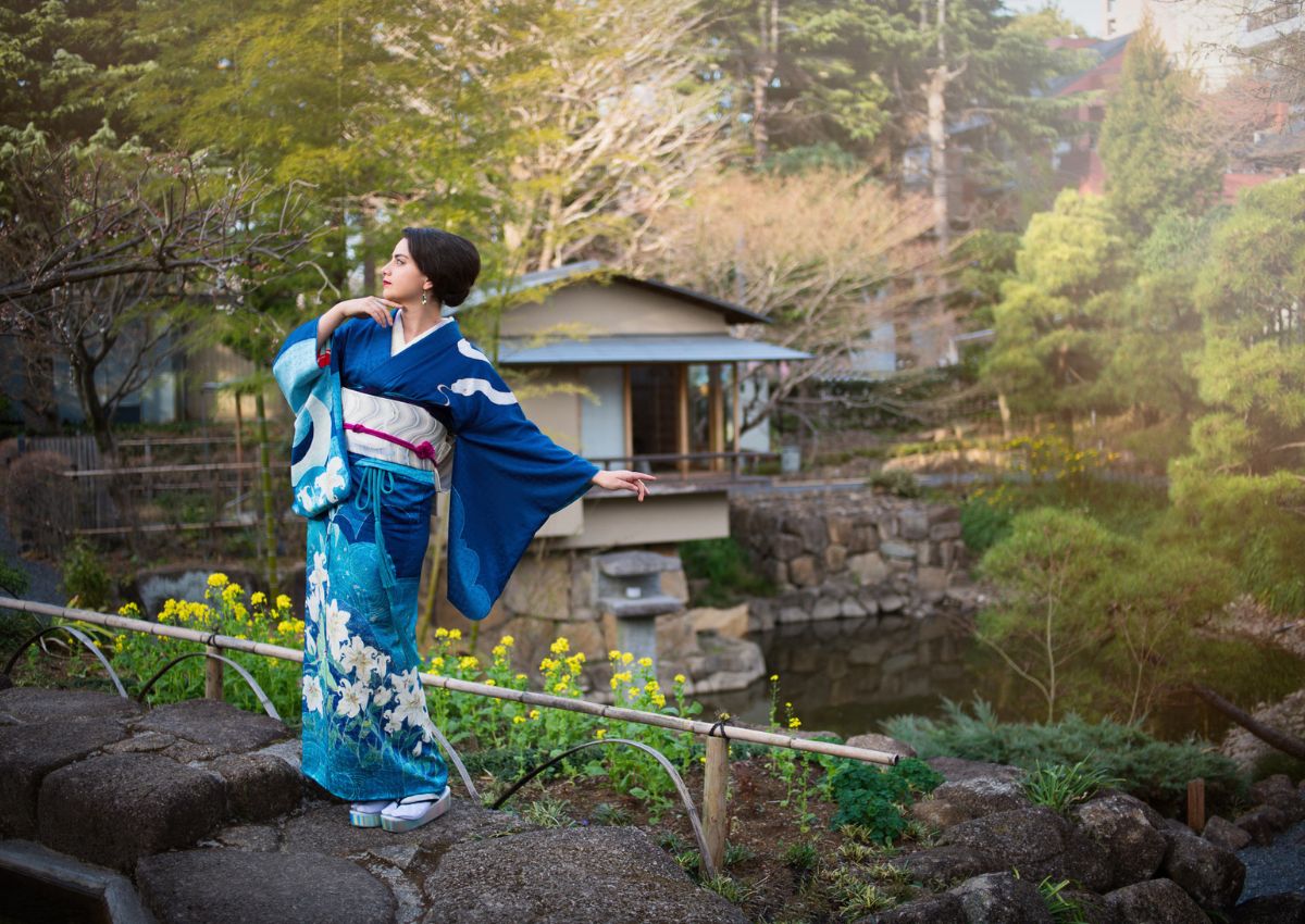 Woman in blue houmongi kimono poses in Japanese tea garden