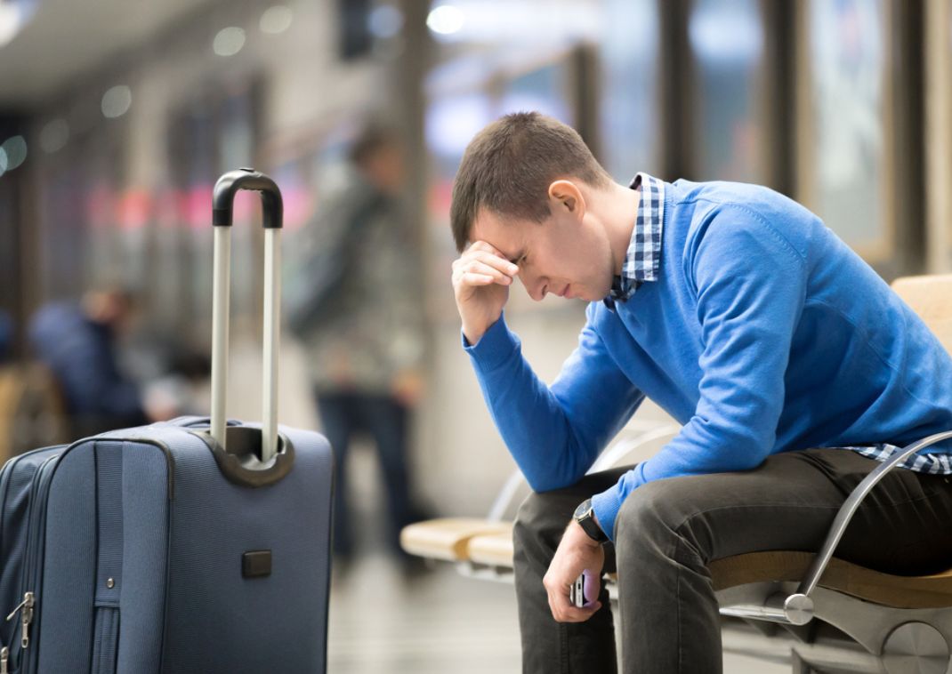 Man at airport with luggage looking disappointed because he missed his flight