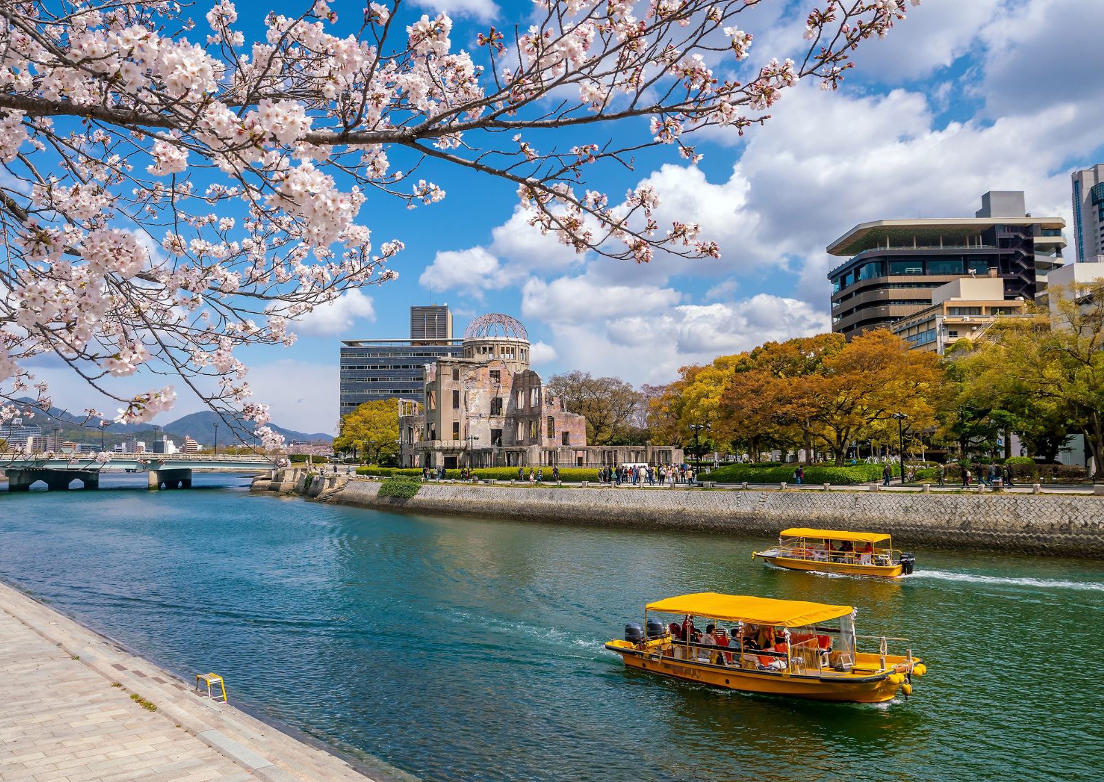 Boats going along the Motoyasu River in Hiroshima on a sunny day with cherry blossoms in front