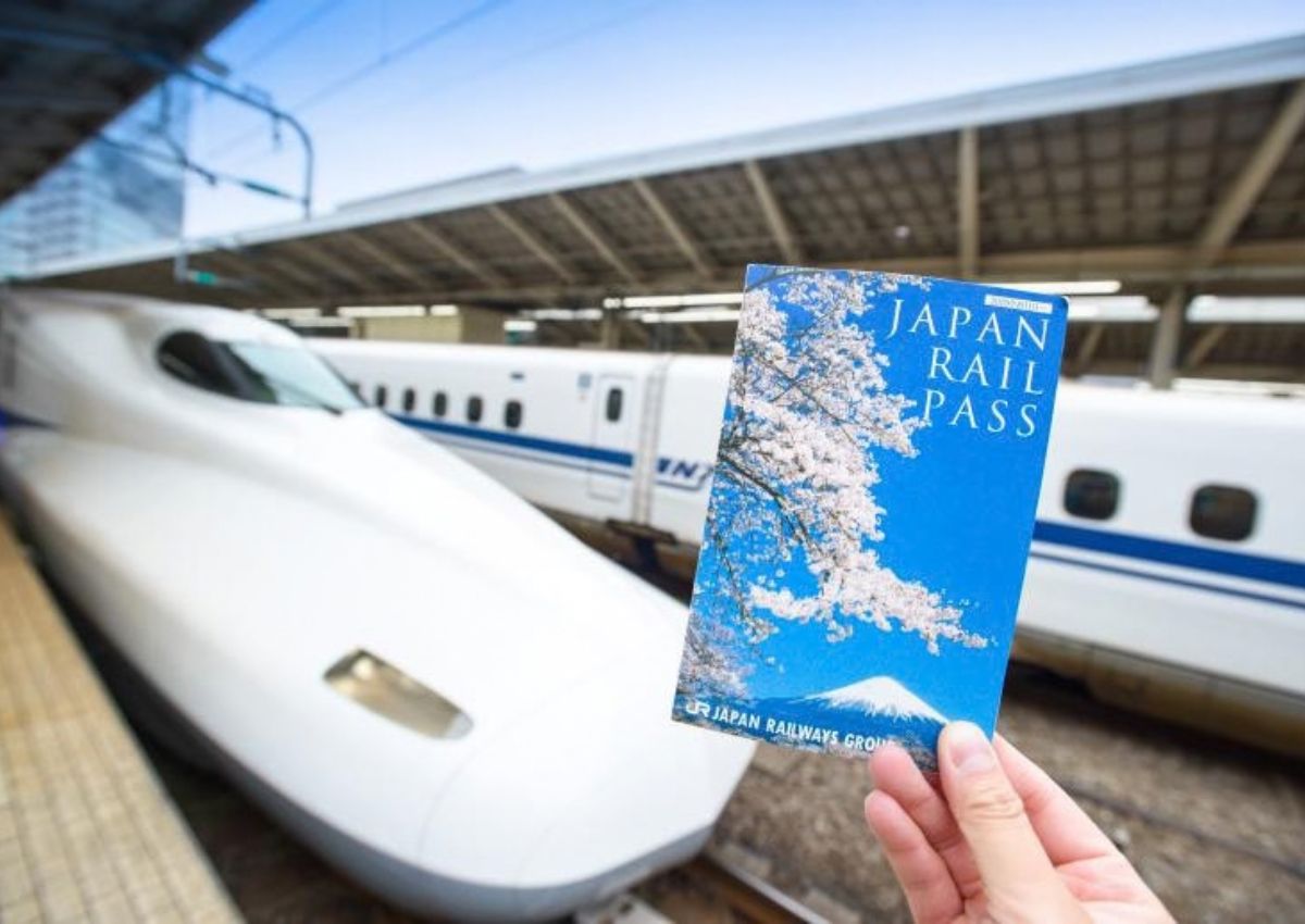 Hand holding a Japan Rail Pass in front of a shinkansen train in Japan
