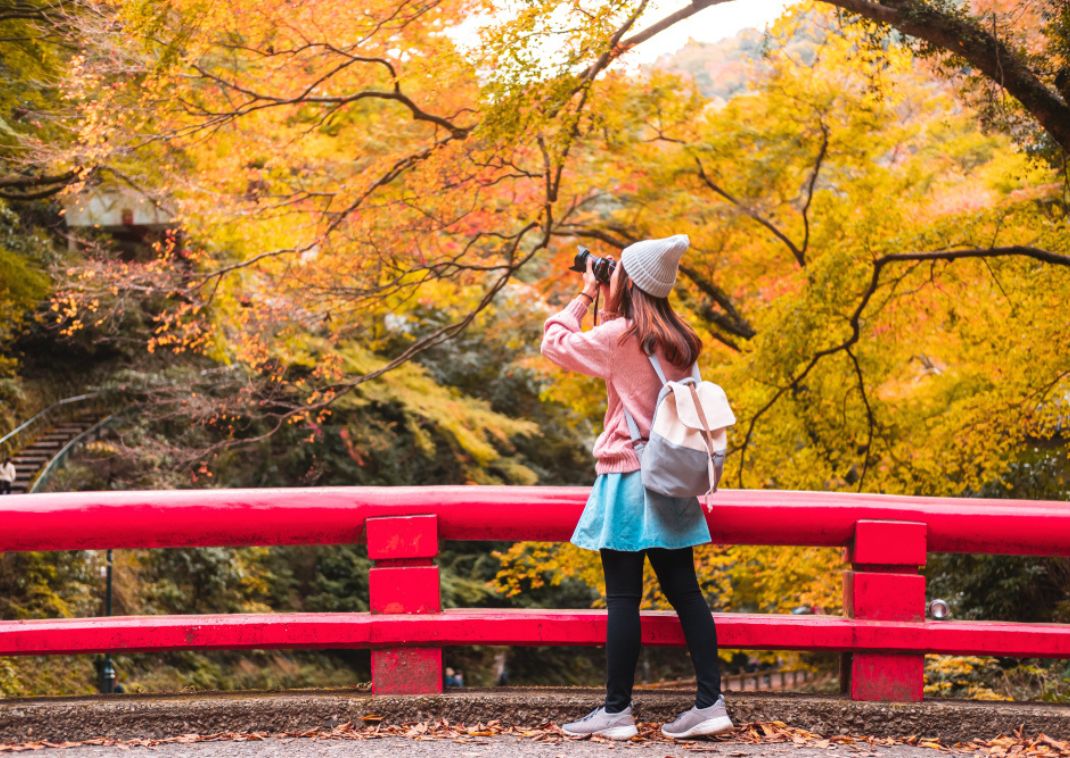 Young woman traveller photographing beautiful autumn in Japan