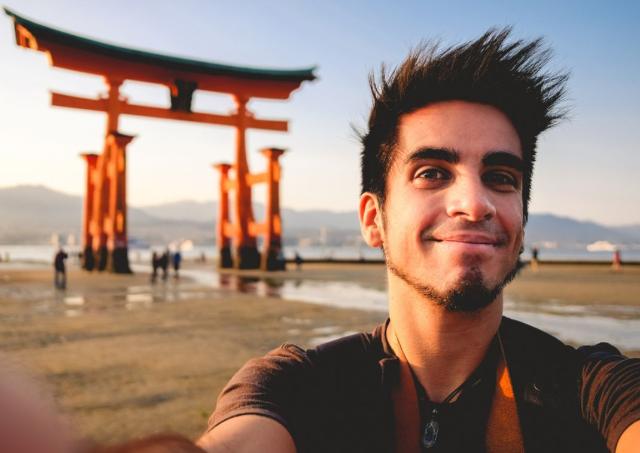 Man standing in front of a red Japanese torii gate in Japan