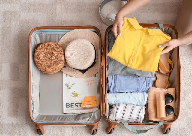 Woman packing yellow shirt into a summery suitcase for a Japan trip 