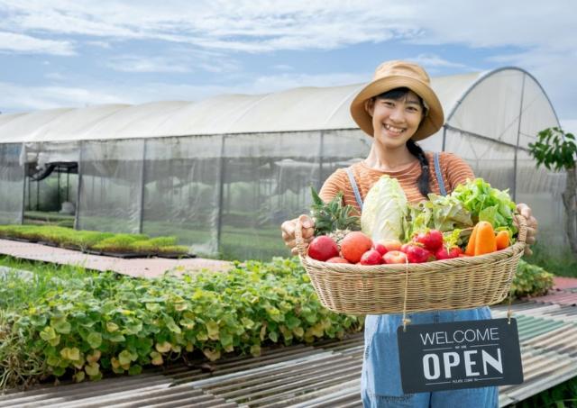 Young Asian female farmer holding large basket of vegetables 