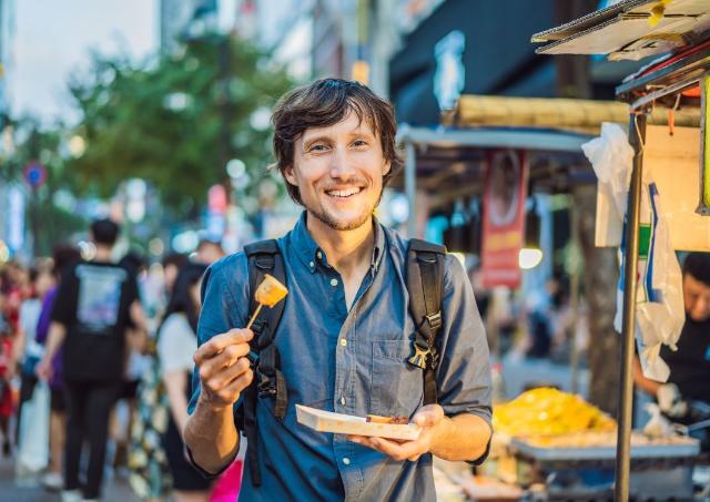 Young man tourist eating Typical Korean street food 