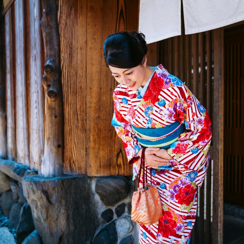 Japanese woman in a colorful kimono bowing in front of a traditional wooden building in Kyoto