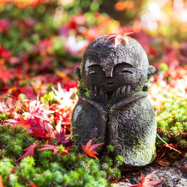 Japanese Jizo sculpture doll with falling Red Maple leaf in Japanese Garden at Enkoji Temple, Kyoto, Japan