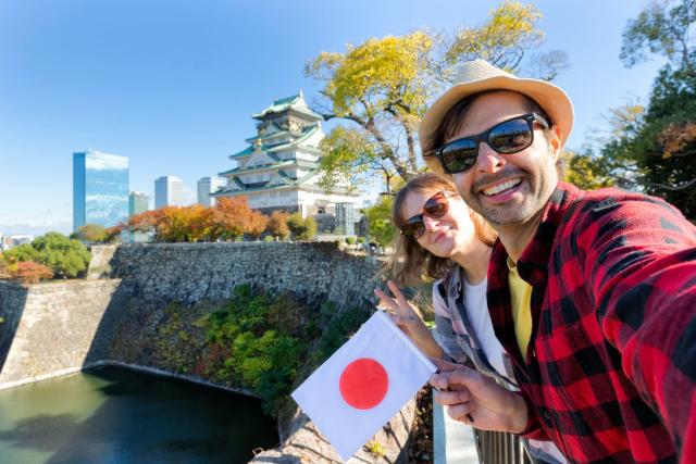 Tourists in Japan holding a japanese flag in front of Osaka castle