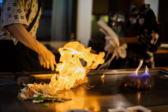 Chef preparing teppanyaki meal with gilled beef and vegetables