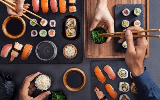 Assorted sushi including nigiri, sashimi, and rolls being shared and eaten with chopsticks