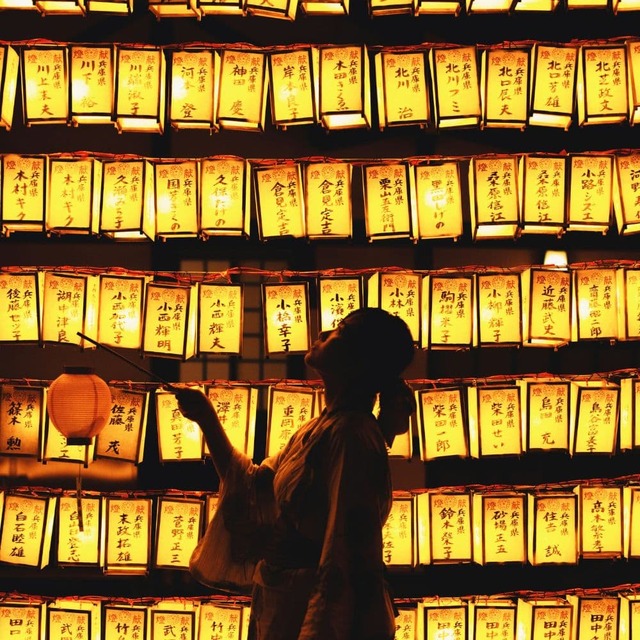 Person with lantern in front of glowing Japanese festival lanterns.