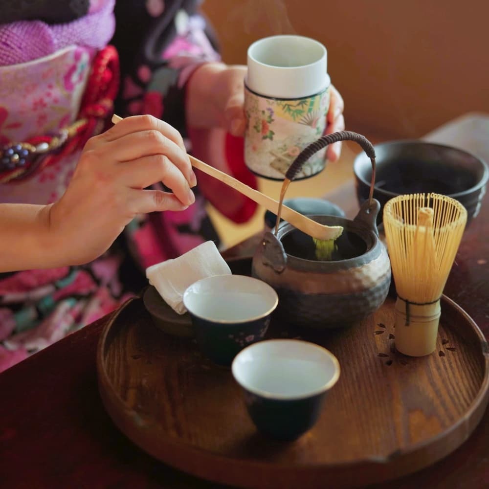 Japanese woman preparing matcha tea in a traditional tea ceremony at home, with matcha powder, herbs, and a teapot