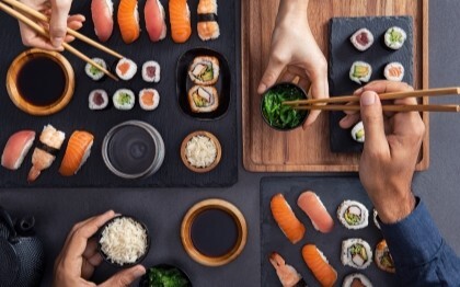 Assorted sushi including nigiri, sashimi, and rolls being shared and eaten with chopsticks