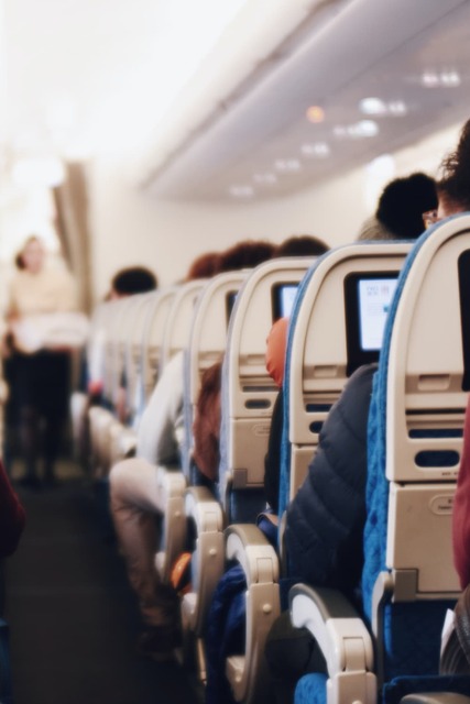 Interior of a large passenger airplane with people seated and a stewardess in uniform walking down the aisle