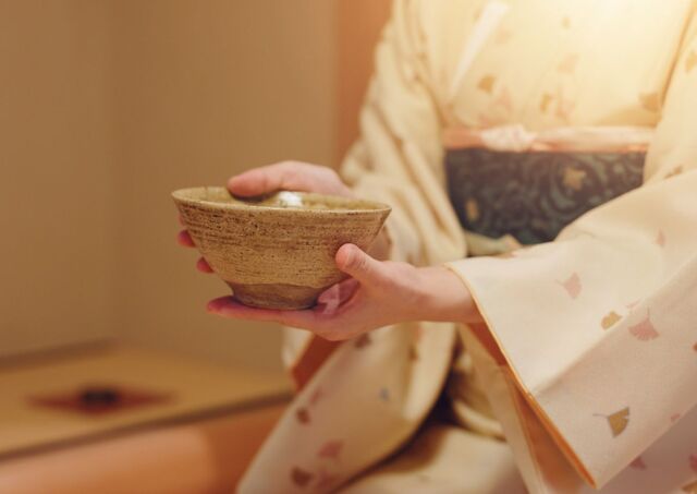 Japanese woman in kinmono handing over tea bowl