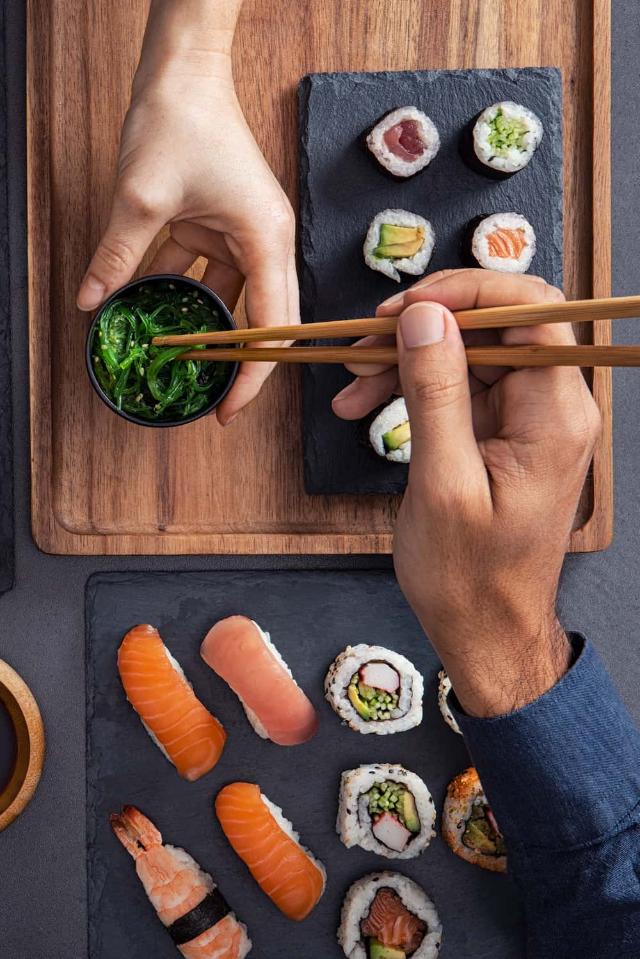 Assorted sushi including nigiri, sashimi, and rolls being shared and eaten with chopsticks