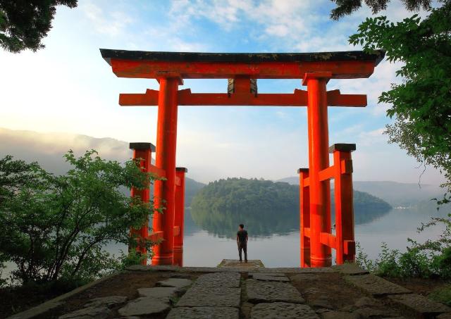 A man standing at red Torii gate of Hakone shintu shrine located on lake Ashi, Japan